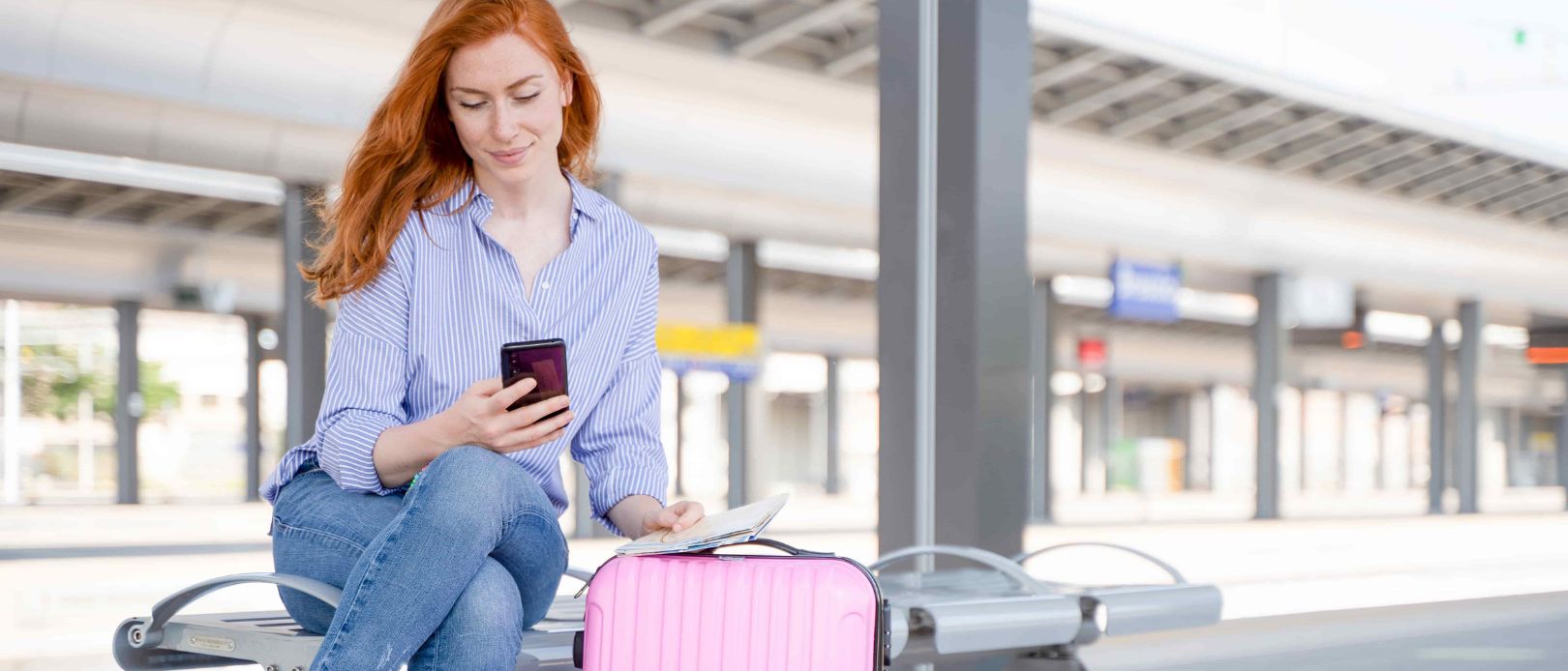 Young woman holding cellphone sitting in train station platform